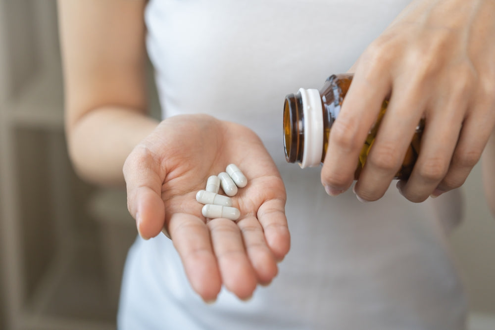 7 best supplements to improve gut health - woman holding 5 capsules and glass bottle