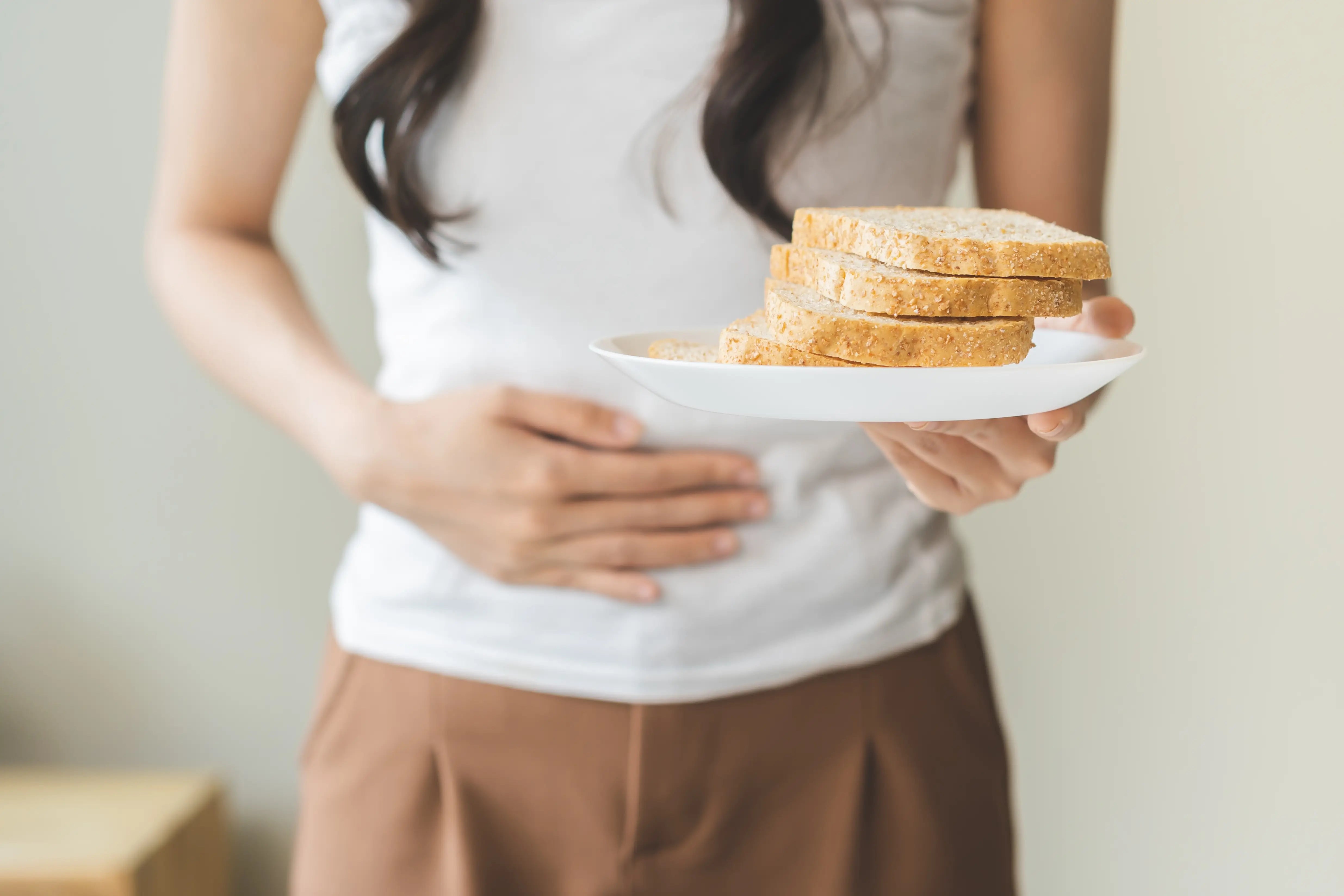 Gluten allergy, asian young woman hand holding, refusing to eat white bread slice on plate in breakfast food meal at home, girl having a stomach ache. Gluten intolerant, coeliac disease, leaky gut syndrome and Gluten free diet concept
