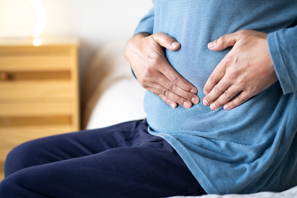 crohns disease - man sitting alone on his bed and suffering from stomach cramps while home alone.Abdominal pain can be caused by digestive problems, infections, intestinal inflammation or more serious diseases.