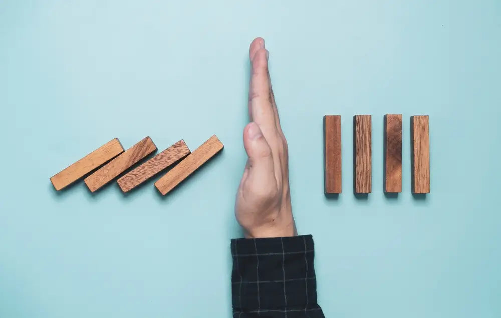 man gesture stop wooden block dominoes falling to standing wooden blocks. prevention measures instead of letting all dominoes fall and then try to cure them