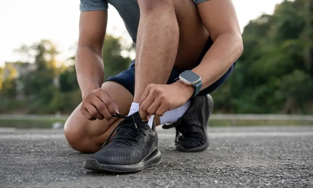 A strong, fit man in sportswear is tying his shoelaces and getting ready before exercising in a park. hobby and healthy lifestyle concepts, close-up image