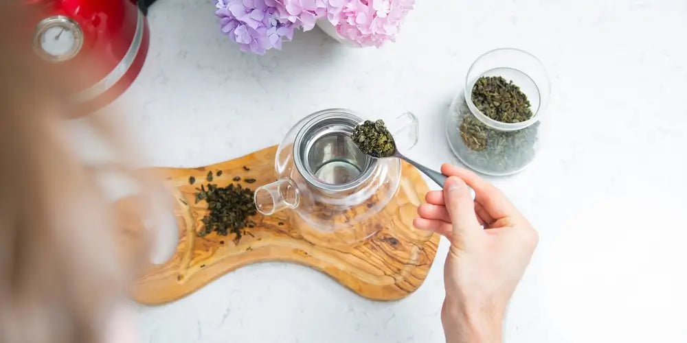 Making a perfect loose tea. Putting tea leaves by a teaspoon into a tea infuser in a glass teapot, top view.