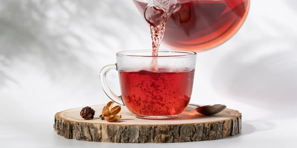 Hot tea is pouring from glass teapot into cup. Hibiscus red tea in glass cup close-up view