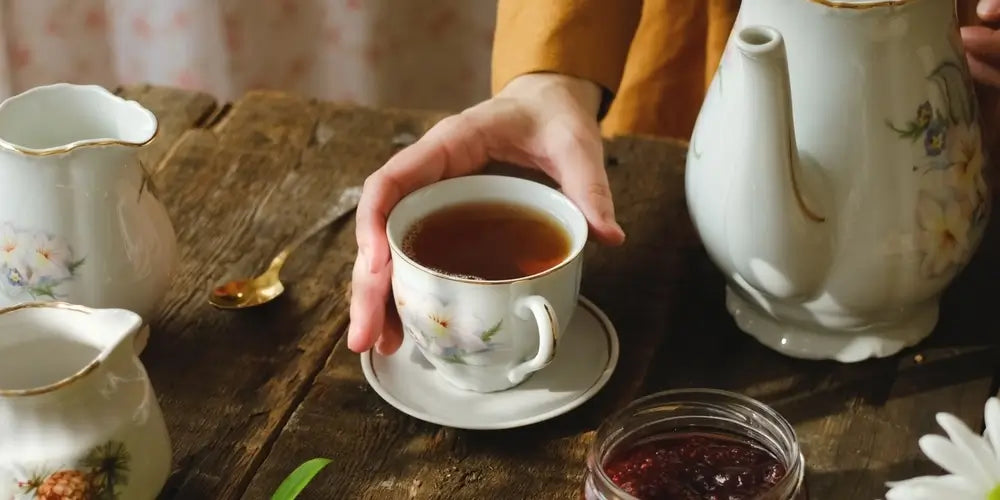 Tea party. Woman drinking tea during morning breakfast. Hand holding cup of black tea on wooden served table.